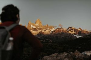 Femme face à une chaine de montagnes ensoleillée.