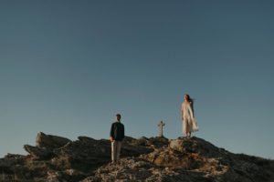 Couple sur les rochers à côté d'une croix.
