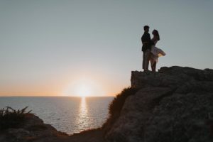 Couple qui s'enlace en haut d'un rocher en bord de mer.