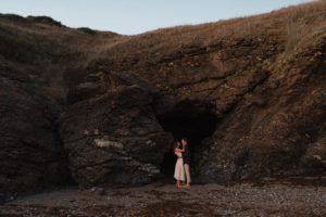 Couple enlacé devant une grotte.