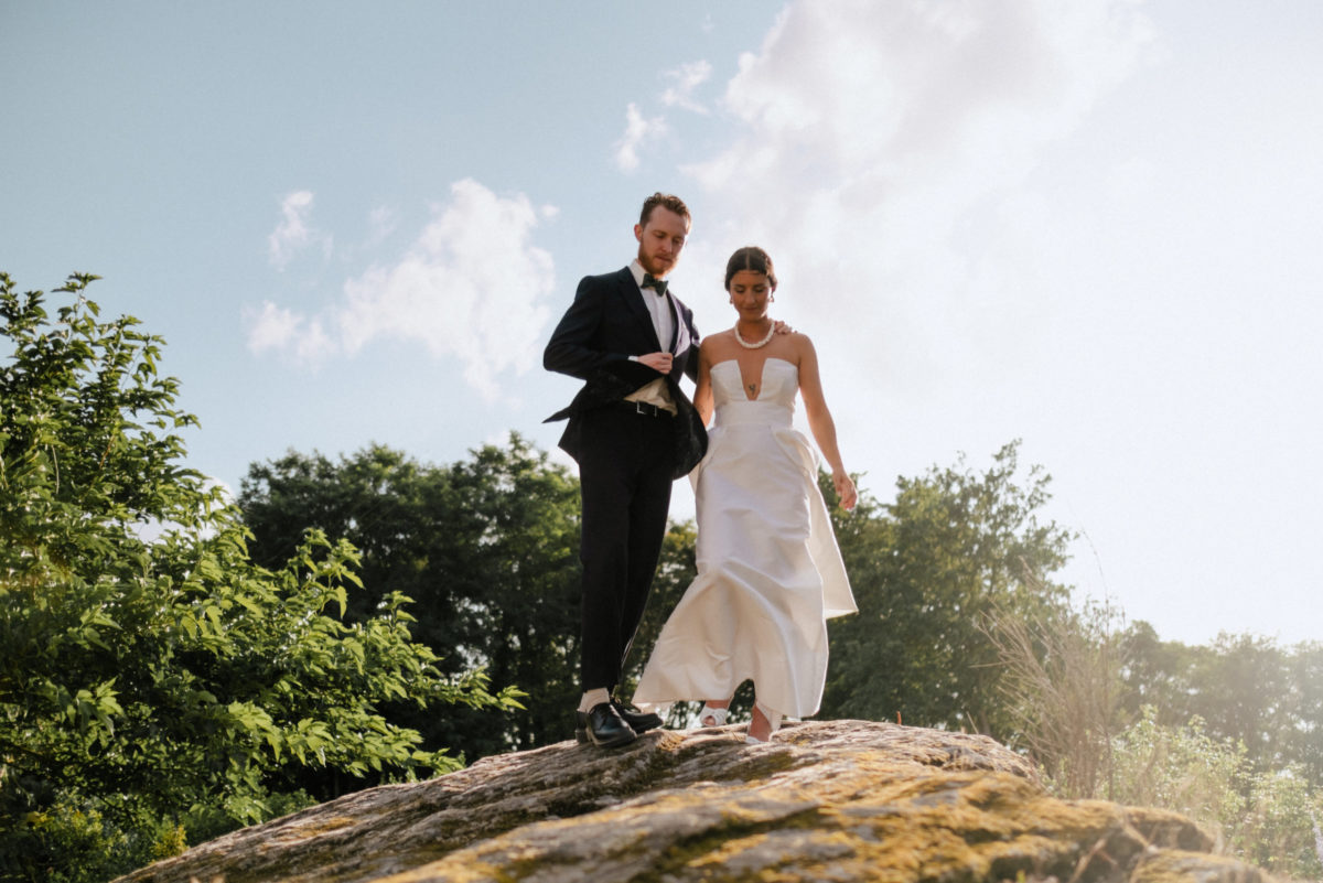 Couple de mariés qui descend d'un roché entouré d'arbres.